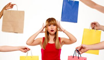 Young beautiful girl standing among purchases with hands on head over white background.